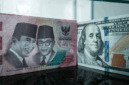 Sejumlah uang kertas pecahan 100.000 rupiah Indonesia difoto di samping uang kertas pecahan 100 dolar AS di sebuah tempat penukaran mata uang di Jakarta, Kamis (4/6/2026). Foto: Yasuyoshi Chiba/AFP