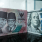 Sejumlah uang kertas pecahan 100.000 rupiah Indonesia difoto di samping uang kertas pecahan 100 dolar AS di sebuah tempat penukaran mata uang di Jakarta, Kamis (4/6/2026). Foto: Yasuyoshi Chiba/AFP
