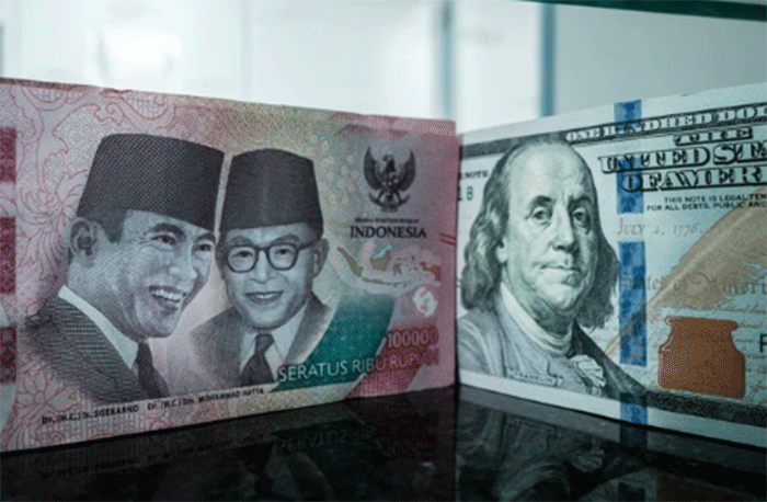 Sejumlah uang kertas pecahan 100.000 rupiah Indonesia difoto di samping uang kertas pecahan 100 dolar AS di sebuah tempat penukaran mata uang di Jakarta, Kamis (4/6/2026). Foto: Yasuyoshi Chiba/AFP