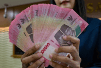 Petugas penukaran uang menunjukkan uang Rupiah di sebuah gerai penukaran mata uang di Jakarta (12/5/2026). Foto: Bay Ismoyo/AFP