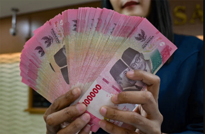 Petugas penukaran uang menunjukkan uang Rupiah di sebuah gerai penukaran mata uang di Jakarta (12/5/2026). Foto: Bay Ismoyo/AFP