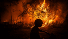 Warga mengendarai sepeda motor saat melintas di samping api yang membakar hutan dan lahan di Kecamatan Sebangau, Kota Palangka Raya, Kalimantan Tengah